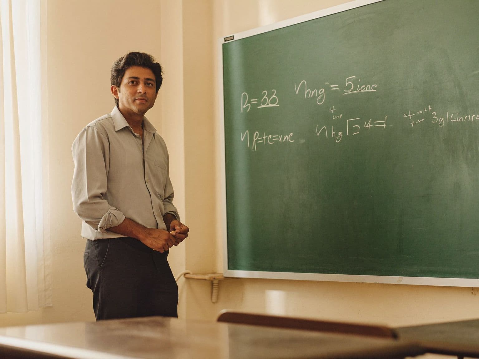 A teacher beside his chalkboard, chalk in hand